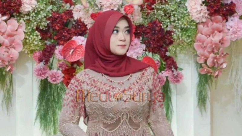 Bu Guru Salsa mengenakan hijab merah dan gaun elegan di depan dekorasi bunga.