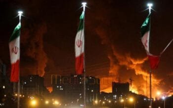 Bendera Iran berkibar saat api dan asap dari serangan Israel terhadap depot minyak Sharan membubung, menyusul serangan Israel terhadap Iran, di Teheran, Iran, 15 Juni 2025. (via REUTERS/Majid Asgaripour)